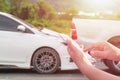 Hand of woman using smartphone and blur of her broken car parking on the road. Contacting car technician, Insurance or need help