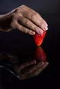 The hand of a woman who takes a strawberry and its reflection with black background Royalty Free Stock Photo