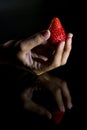 The hand of a woman who takes a strawberry and its reflection with black background Royalty Free Stock Photo