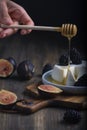 Hand with wooden spoon is pouiring with honey soft cheese, bramble and fig halfs on a rustic board. Close up dark moody shot,