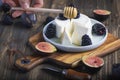 Hand with wooden spoon is pouiring with honey soft cheese, bramble and fig halfs on a rustic board. Close up dark moody shot,