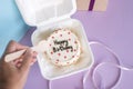 A hand with a wooden spoon reaches for a festive bento cake near the gift box