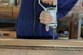 Hand of worker drills a hole with wooden plank using electric drill machine in workshop