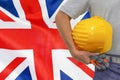 Hand of worker and yellow hard-hat on background flag of UK Royalty Free Stock Photo