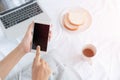 Hand of working woman holding and touching the black smartphone screen. Asian woman sitting on a white cloth while having bread,