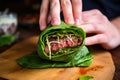 hand wrapping grilled burger in a lettuce leaf