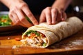 hand wrapping a rolled pita bread with chicken filling