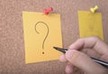 Hand writeing question mark on sticky note or post is on cork