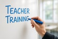 A hand writes \'Teacher Training\' in blue marker on a white board, concept of education Royalty Free Stock Photo