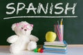 Hand writing on a blackboard in a language class with the word `Spanish` wrote on. Some books and school materials