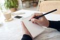 A hand writing down on a white blank notebook with coffee cup and dessert on table in cafe Royalty Free Stock Photo