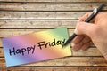 Hand writing Happy Friday with a pencil on a colored sheet over a wooden table