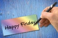 Hand writing Happy Friday with a pencil on a colored sheet over a wooden table