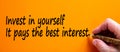 Hand writing `invest in yourself it pays the best interest`, isolated on orange background. Business concept, copy space