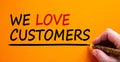 Hand writing `we love customers`, isolated on beautiful orange background. Business concept, copy space