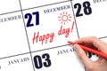 Hand writing the text HAPPY DAY and drawing the sun on the calendar date December 27