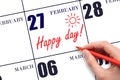 Hand writing the text HAPPY DAY and drawing the sun on the calendar date February 27