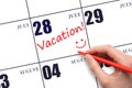 A hand writing a VACATION text and drawing a smiling face on a calendar date 28July. Vacation planning concept.