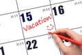 A hand writing a VACATION text and drawing a smiling face on a calendar date 15July. Vacation planning concept. Royalty Free Stock Photo