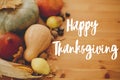 Hand written Happy Thanksgiving text on background of pumpkins, autumn leaves, nuts, harvest vegetables on rustic wooden table. Royalty Free Stock Photo