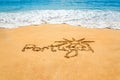 Hand written text Portugal and sun symbol on the golden beach sand with coming waves