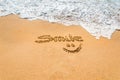 Hand written text smile and symbol on the golden beach sand with coming wave Royalty Free Stock Photo