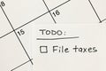Hand written to-do list with \'File taxes\' reminder written on a sticky note over a calendar