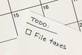 Hand written to-do list with \'File taxes\' reminder on a sticky note over a calendar