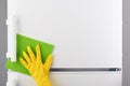 Hand in yellow glove cleaning white refrigerator with green rag Royalty Free Stock Photo