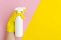 Hand with yellow glove holding a spay bottle closeup on bright split color background. Pink and yellow vibrant duotone Royalty Free Stock Photo