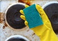 Hand in yellow glove holding washup sponge against dirty electric stove