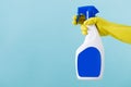 Hand in yellow glove holds spray bottle of liquid detergent on blue background. cleaning Royalty Free Stock Photo