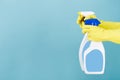 Hand in yellow glove holds spray bottle of liquid detergent on blue background. cleaning Royalty Free Stock Photo