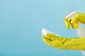 Hand in yellow glove holds spray bottle of liquid detergent and sponge on blue background. cleaning Royalty Free Stock Photo