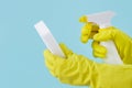 Hand in yellow glove holds spray bottle of liquid detergent and sponge on blue background. cleaning Royalty Free Stock Photo