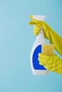 Hand in yellow glove holds spray bottle of liquid detergent and sponge on blue background. cleaning Royalty Free Stock Photo