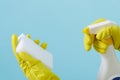 Hand in yellow glove holds spray bottle of liquid detergent and sponge on blue background. cleaning Royalty Free Stock Photo