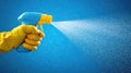 A hand in a yellow glove sprays a cleaning solution against a blue background Royalty Free Stock Photo