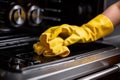 a hand in a yellow glove washes stains electric stove in the kitchen generative ai