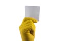 A hand in a yellow latex glove holds a white square sheet of paper