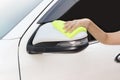 Hand with yellow microfiber cloth cleaning big white side mirror