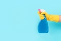 Hand in yellow protective rubber glove holding spray bottle with detergent against blue background with copy space Royalty Free Stock Photo