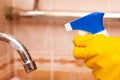 hand in a yellow rubber glove disinfects the water faucet in the bathroom