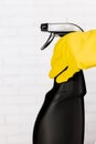 Hand in yellow rubber glove holding black plastic spray detergent bottle. Household chemicals. Cleaning product Royalty Free Stock Photo