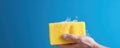 A Hand In A Yellow Rubber Glove Holding A Cleaning Sponge And Wiping Soapy Foam On A Blue Background Representing Cleaning And Royalty Free Stock Photo