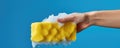 A Hand In A Yellow Rubber Glove Holding A Cleaning Sponge And Wiping Soapy Foam On A Blue Background Representing Cleaning And Royalty Free Stock Photo