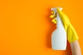 Hand in yellow rubber glove holding plastic spray bottle with cleaning detergent on a orange background Royalty Free Stock Photo