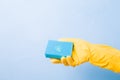 hand in a yellow rubber glove holds a blue sponge with a drop of green dishwashing gel