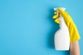 Hand in a yellow rubber glove holds cleaner spray bottle over blue background. Cleaning service banner mockup. Housecleaning and Royalty Free Stock Photo