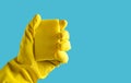 Hand with yellow rubber glove holds a sponge on a blue background, copy space. Royalty Free Stock Photo